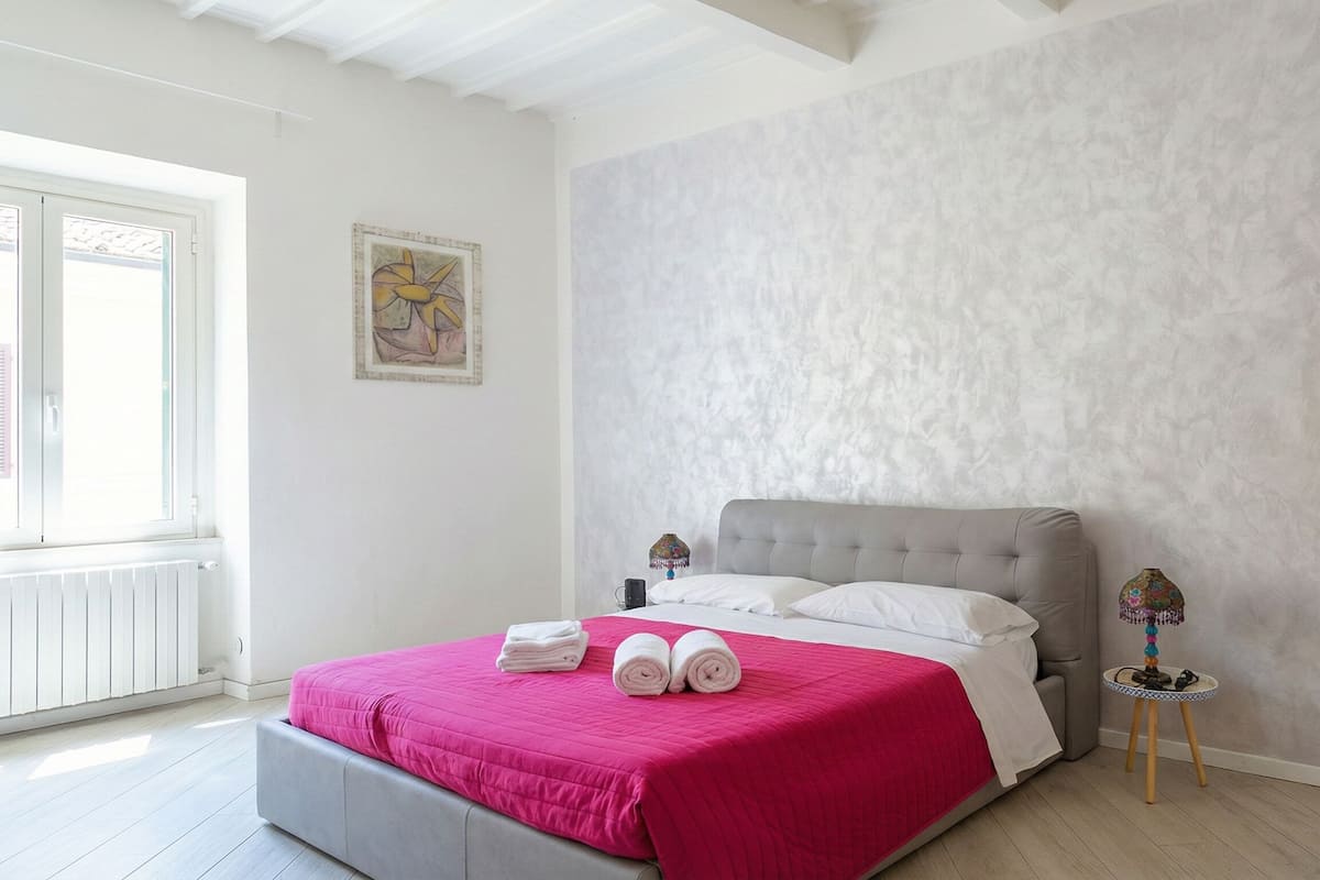 A bedroom with a bed, a window, a radiator, and a wall-mounted artwork.
