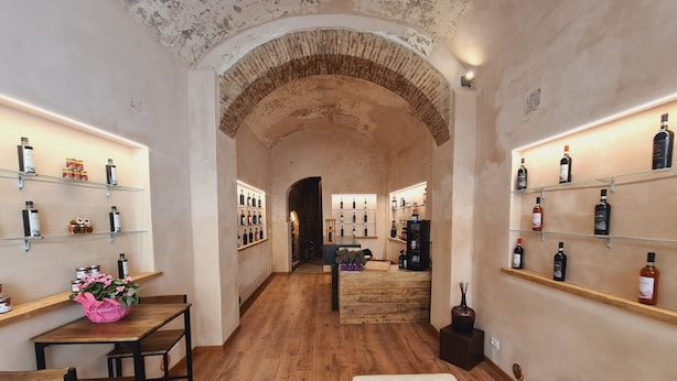 Un pasillo con suelo de madera, un banco acolchado blanco y estanterías a ambos lados exhibiendo botellas.