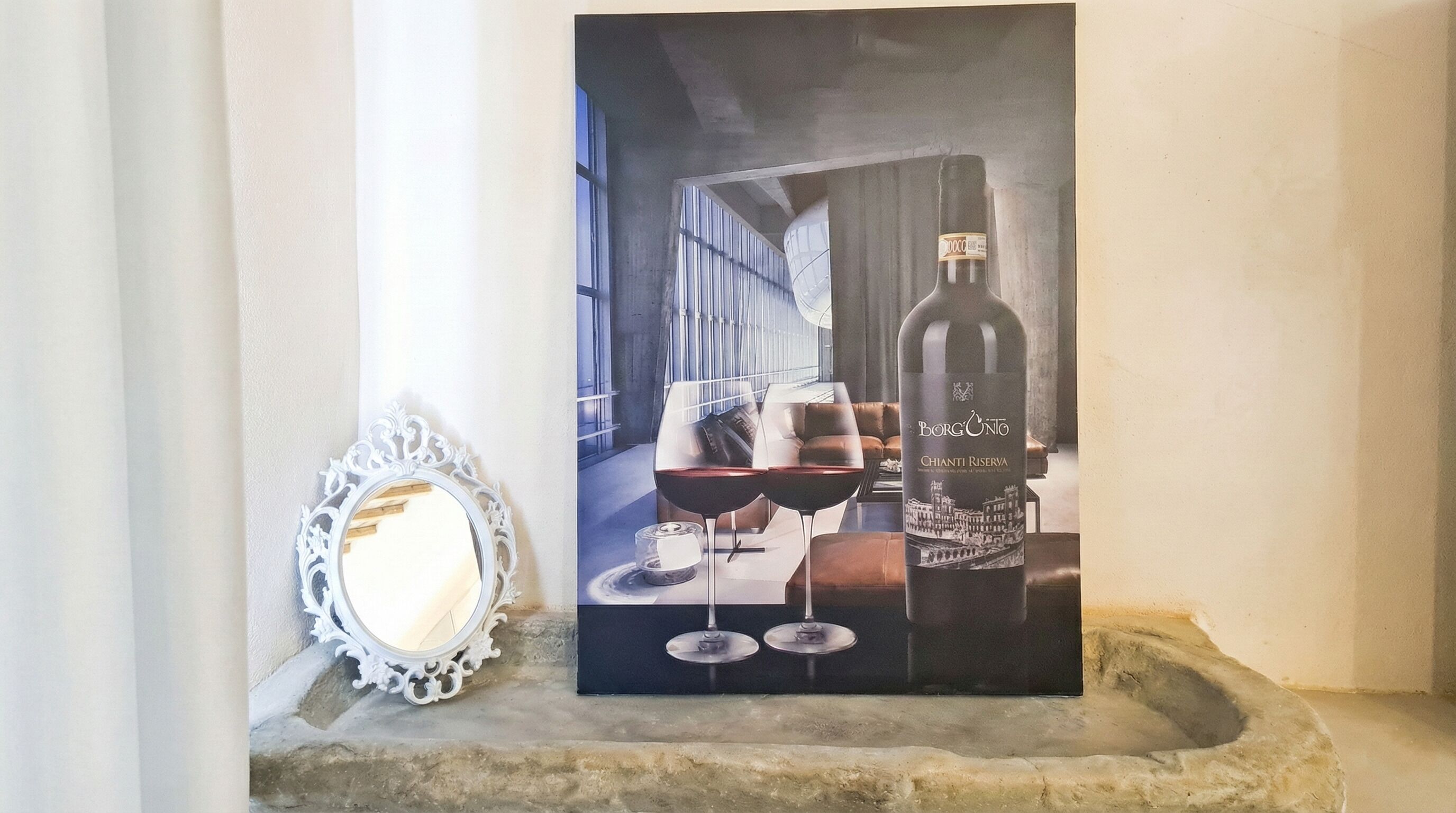 A framed artwork of a wine bottle and glasses on a stone ledge.