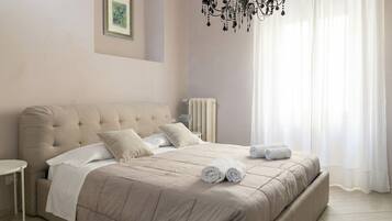 A bedroom with a large bed, a bedside table, a radiator, and a chandelier.