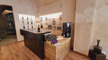 Un espace d’accueil avec un comptoir en bois, des étagères remplies de boissons en bouteille, un réfrigérateur noir et un vase décoratif.