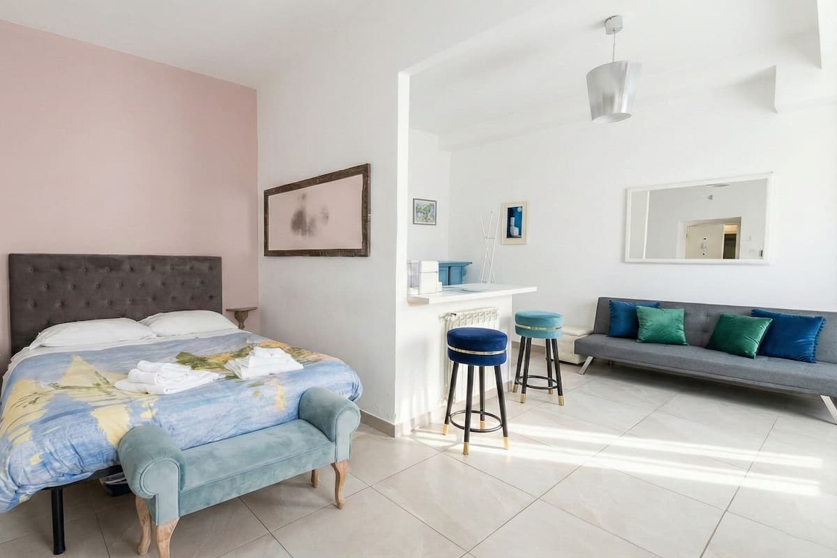 A bedroom with a bed, a sofa, a small bar area, and a mirror.