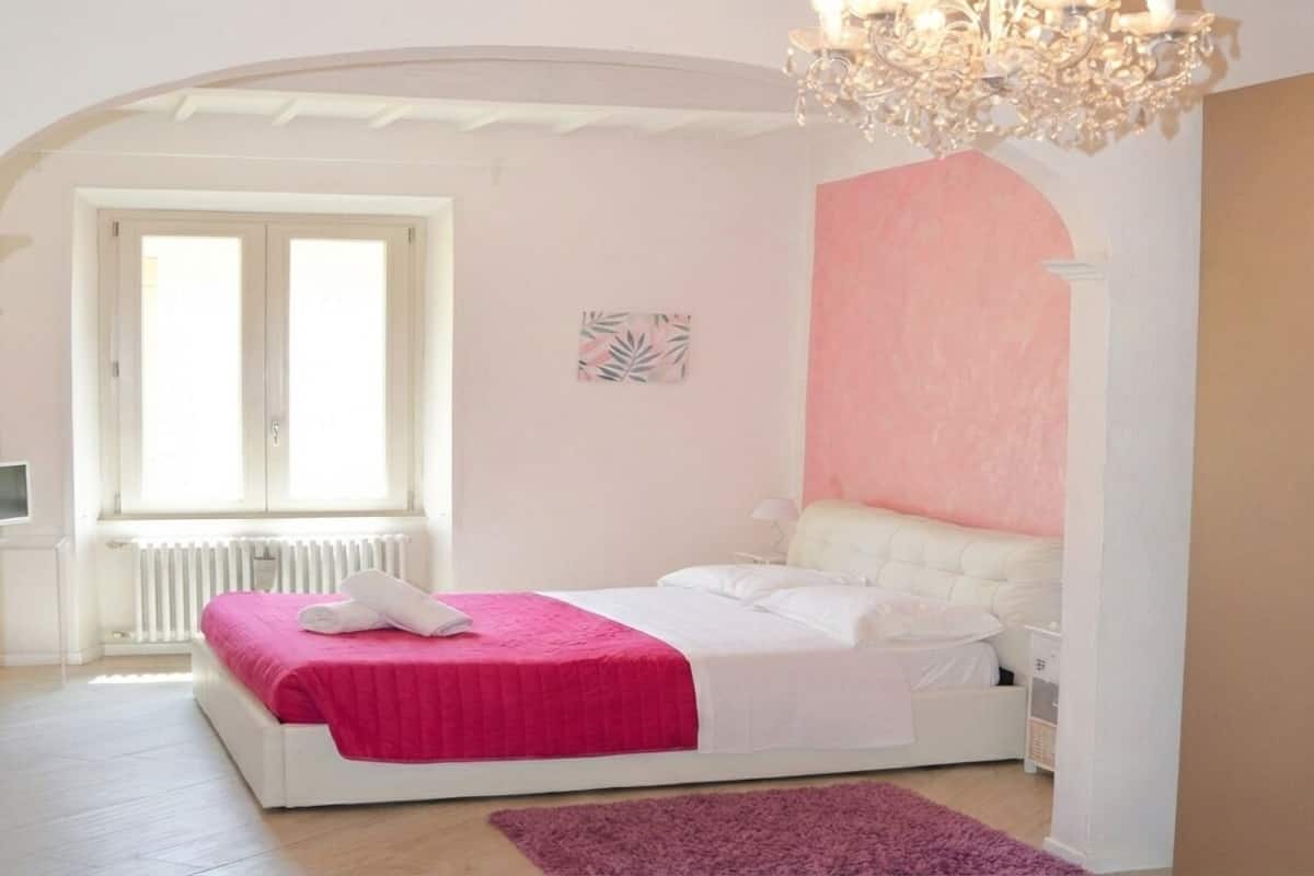 A bedroom with a bed, a window, a radiator, and a chandelier.