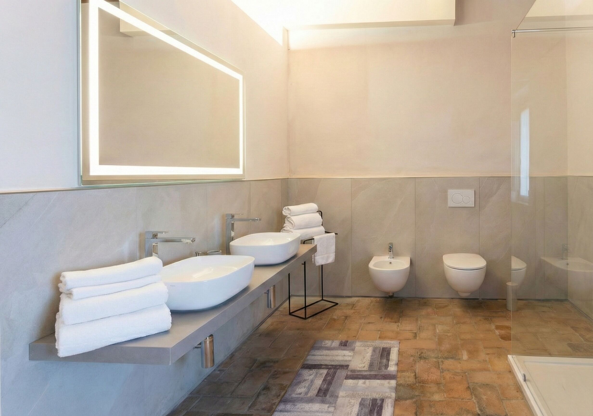 A modern bathroom with a large mirror, two sinks, a bidet, and a shower.