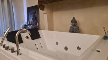 Une salle de bain moderne avec une grande baignoire blanche, une douchette à main et une petite statue de Bouddha.
