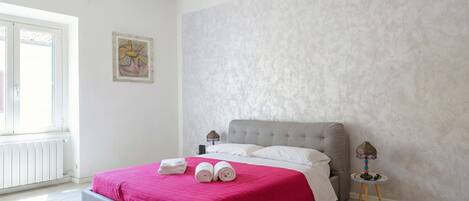 Un dormitorio con una cama tapizada en gris, ropa de cama blanca, una colcha rosa y una sola obra de arte en la pared.
