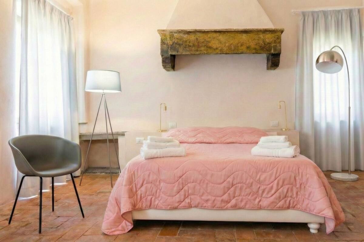 A bedroom with a bed, a chair, a lamp, and a window with curtains.