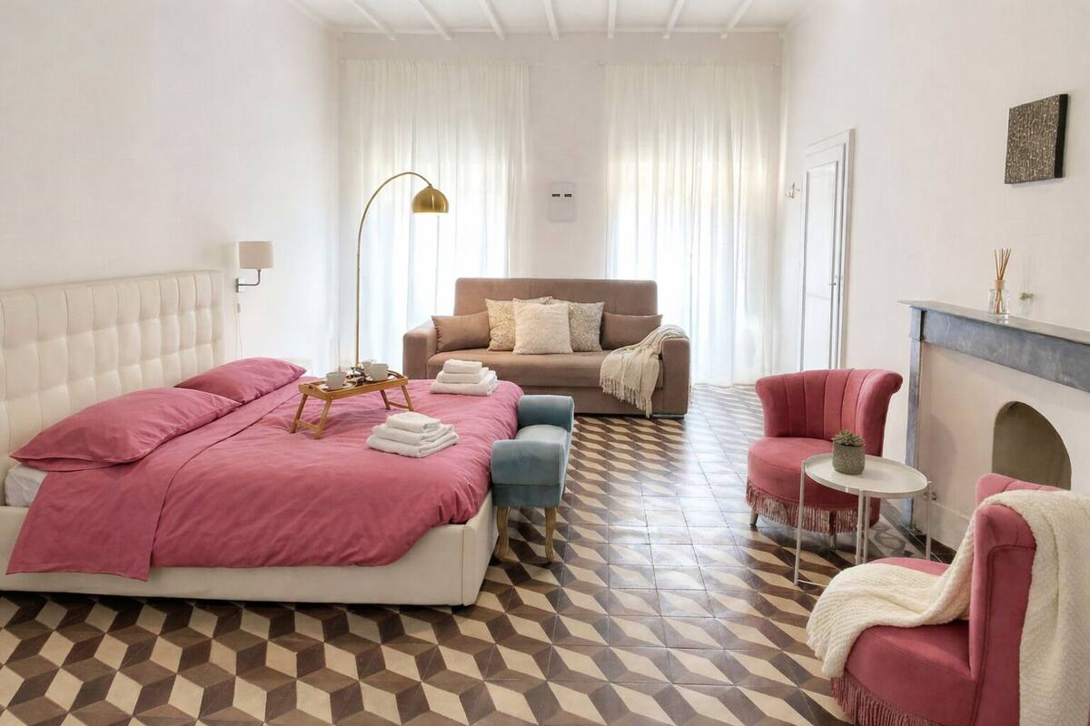 A hotel room with a bed, a sofa, a chair, a small table, and a fireplace.
