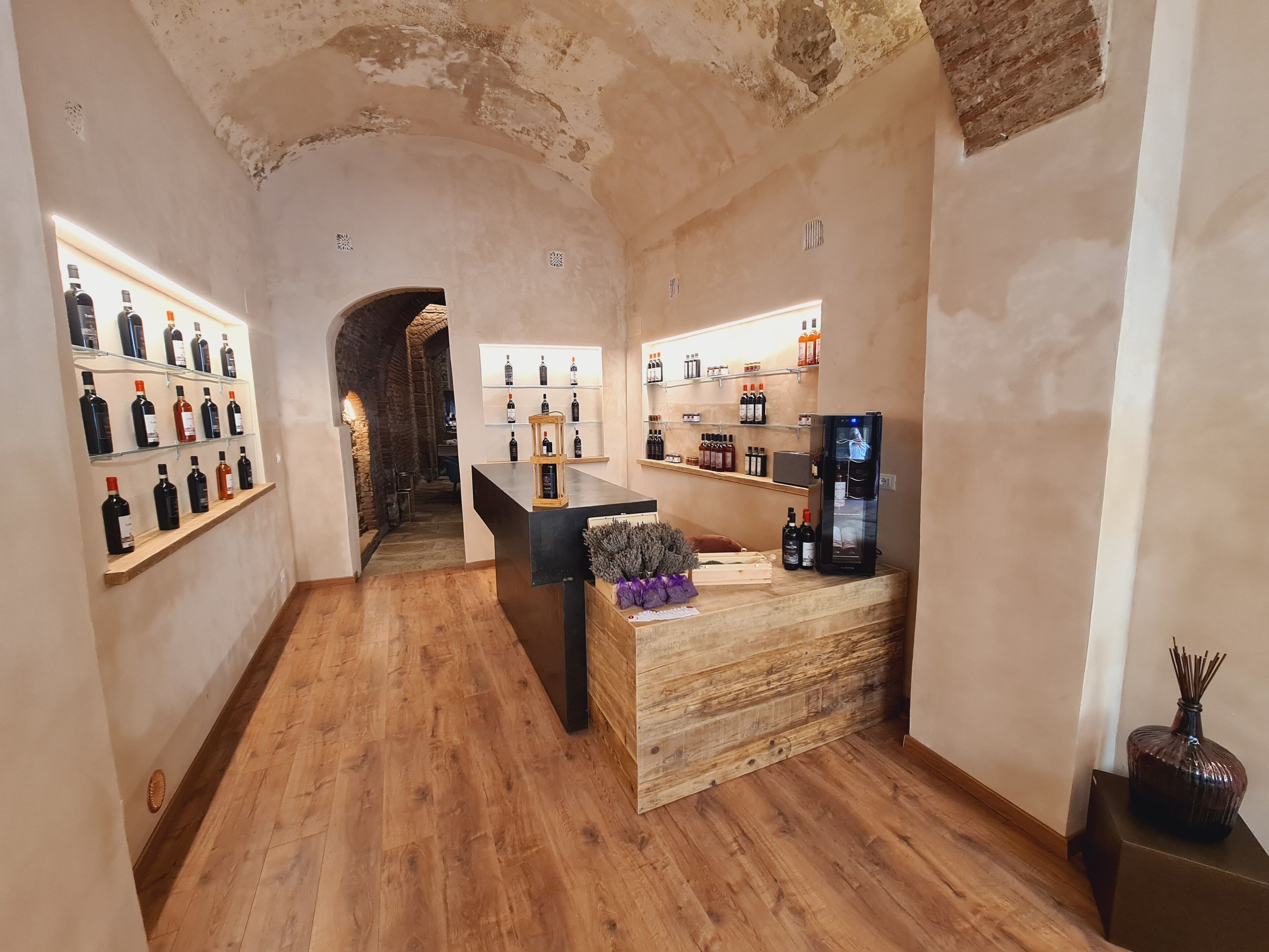 A wine tasting room with wooden floors, a central tasting table, and shelves of wine bottles on either side.