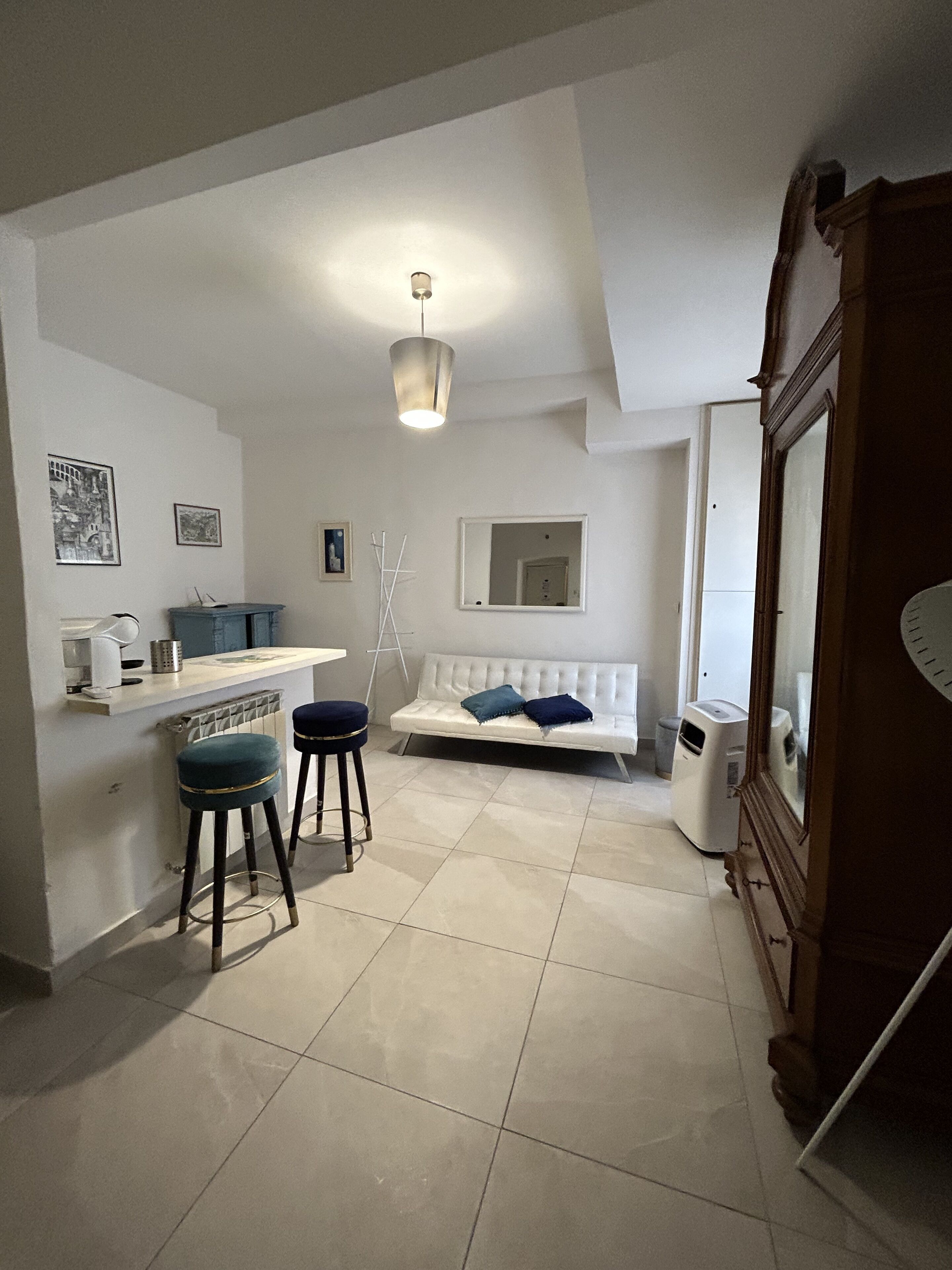 A compact kitchen with a dining area, a white sofa, and a small bar stool.