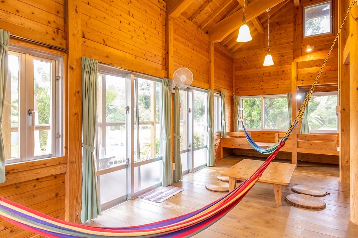 L’intérieur d’un chalet en bois, avec de grandes fenêtres, un hamac et un banc en bois.