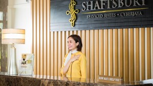 Una recepción con un cartel que dice "SHAFTSBURY SERVICED SUITES • CYBERJAYA" y un cartel con la inscripción "¿En qué puedo ayudarle?" debajo.