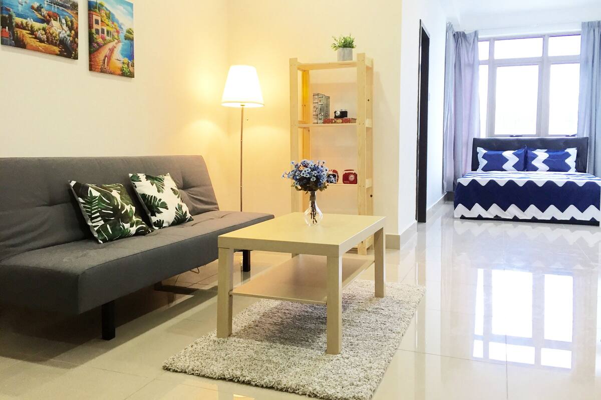 A modern living room with a grey sofa, a wooden coffee table, and a small bookshelf.