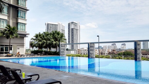 Una piscina en la azotea con sillones de descanso, palmeras y edificios altos al fondo.