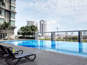 A rooftop pool with lounge chairs, palm trees, and high-rise buildings in the background. - Cyberjaya Studio Suites (Cyberjaya)