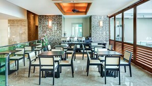 Un comedor espacioso con techos altos, paredes de granito y ventanas grandes. Mesas y sillas dispuestas para comer.