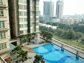 A modern building with a swimming pool, palm trees, and high-rise buildings in the background. - Cyberjaya Studio Suites (Cyberjaya)