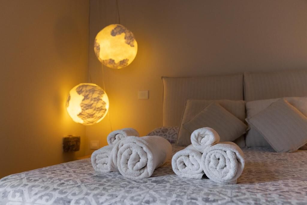 A neatly made bed with rolled towels and two wall-mounted lamps.
