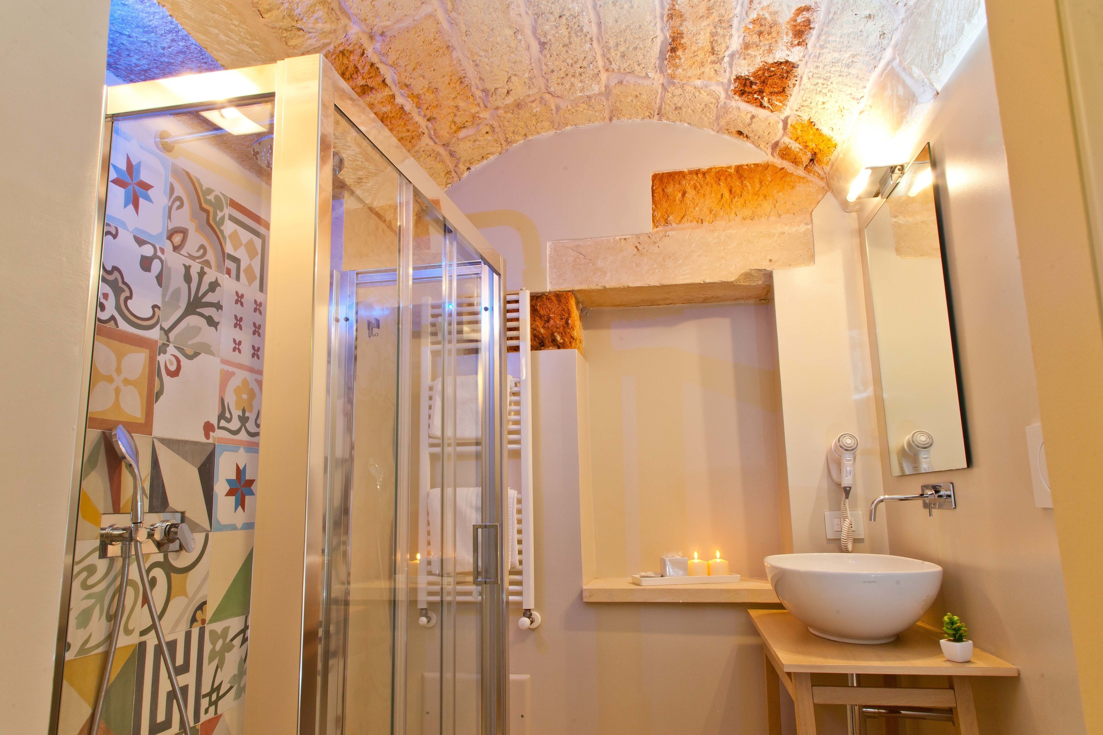 A bathroom with a glass-enclosed shower, a white sink with a mirror, and a tiled wall with a geometric pattern.