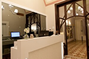 Una mesa de recepción con una computadora, un florero y un espejo grande.