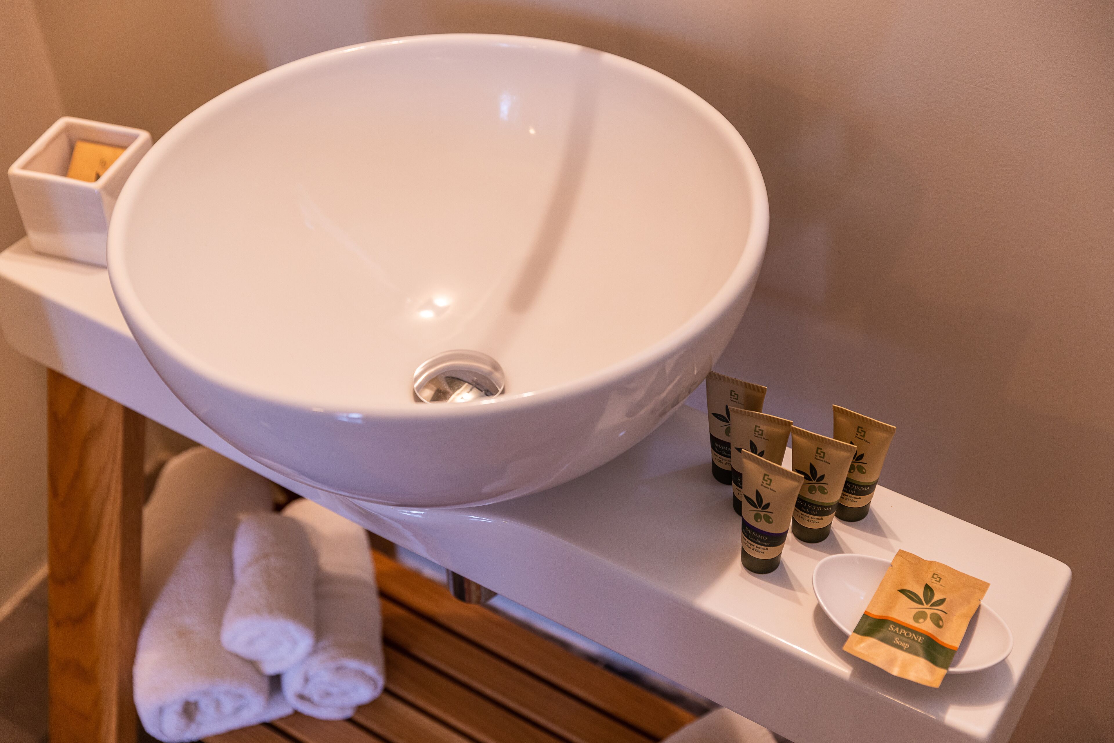 A bathroom with a large white sink, a wooden bench, and several toiletries on the counter.