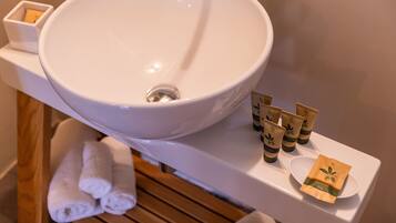 A bathroom with a large white sink, a wooden bench, and several toiletries on the counter.