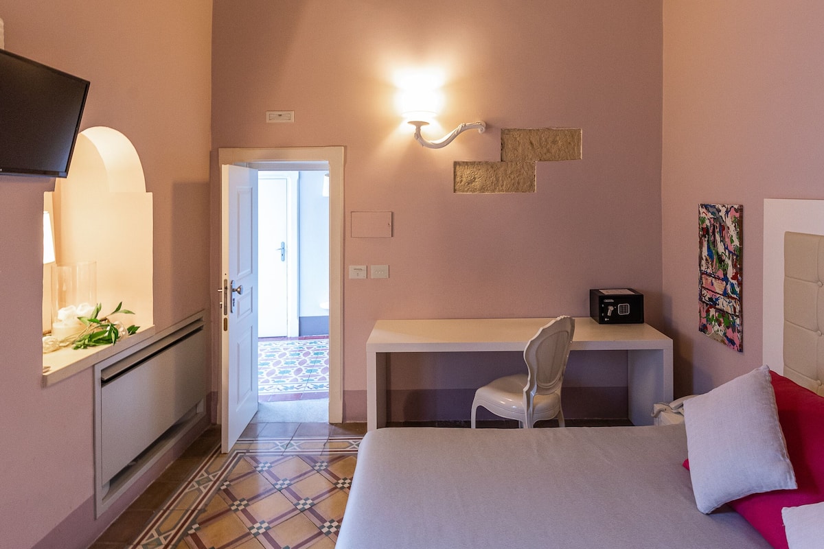 Une chambre d’hôtel équipée d’un lit, d’un bureau, d’une chaise, d’une télévision et d’une porte donnant sur une autre pièce.