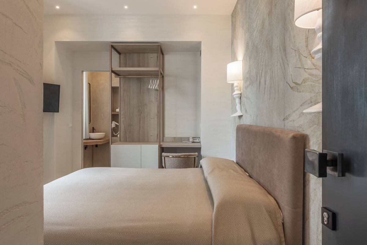 Une chambre d’hôtel moderne, dotée d’un grand lit, d’une coiffeuse en bois, d’un miroir et d’une lampe fixée au mur.