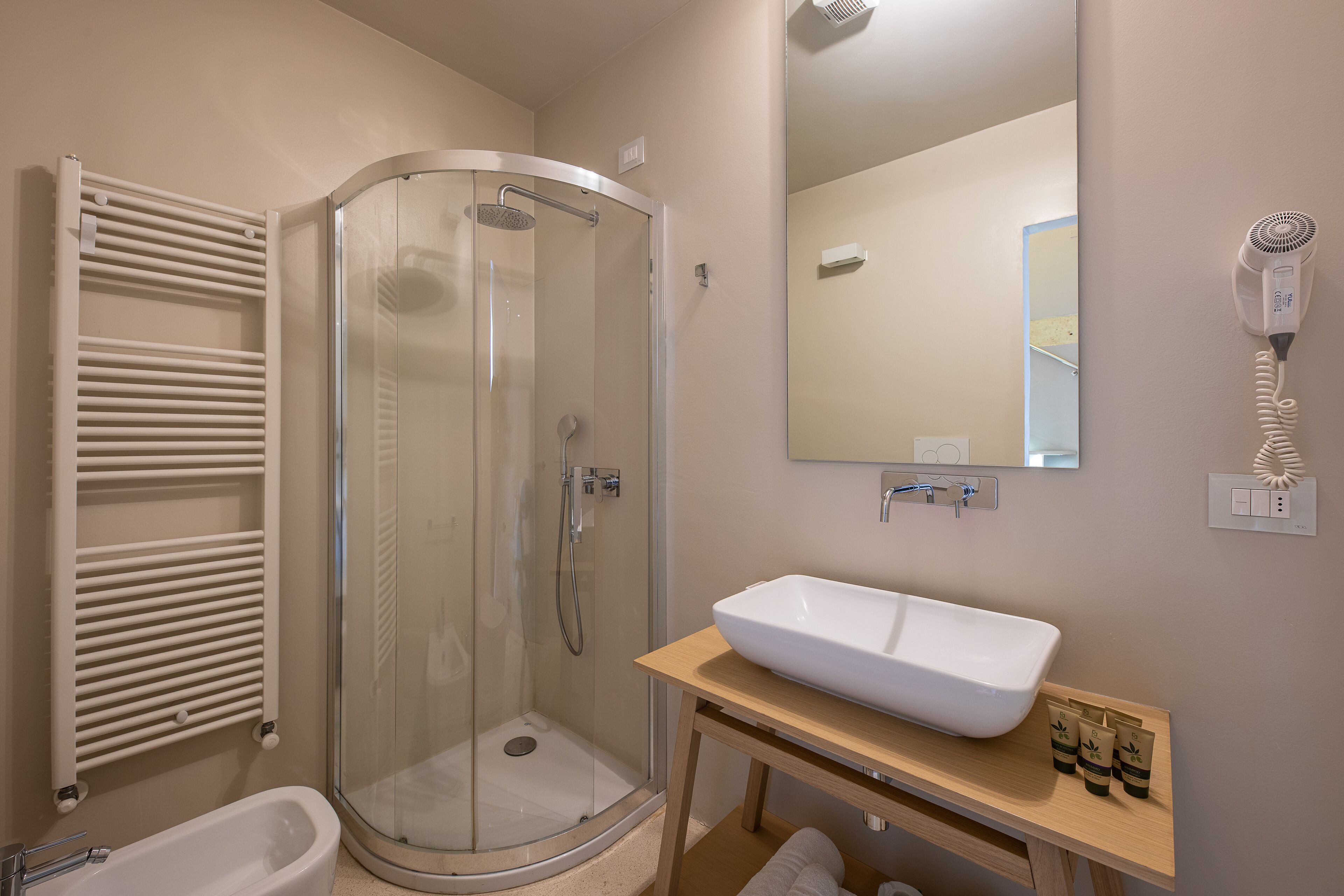 A modern bathroom with a glass-enclosed shower, a white bathtub, and a wooden vanity with a large sink.
