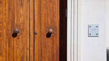 A wooden double door with ornate metal handles and a plaque on the adjacent wall.