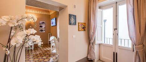 A hallway with a tiled floor, a white chair, a mirror, and a door with curtains.