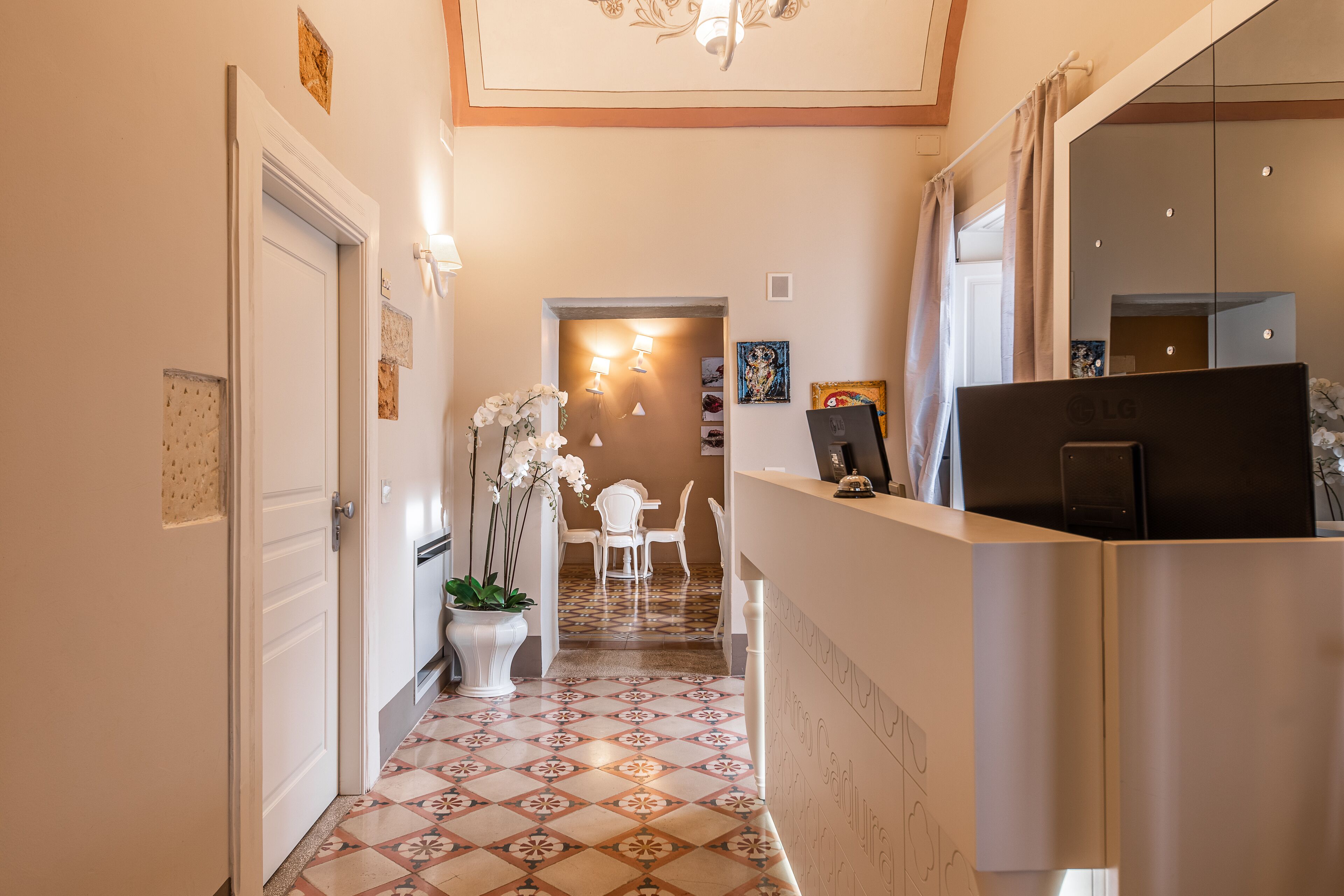 Un passadís amb paviment estampat, una recepció i una zona de dinar amb cadires i una taula.
