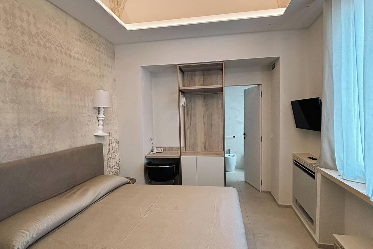 Une chambre à coucher avec un grand lit, un bureau, une télévision et une salle de bain visible à travers une porte ouverte.