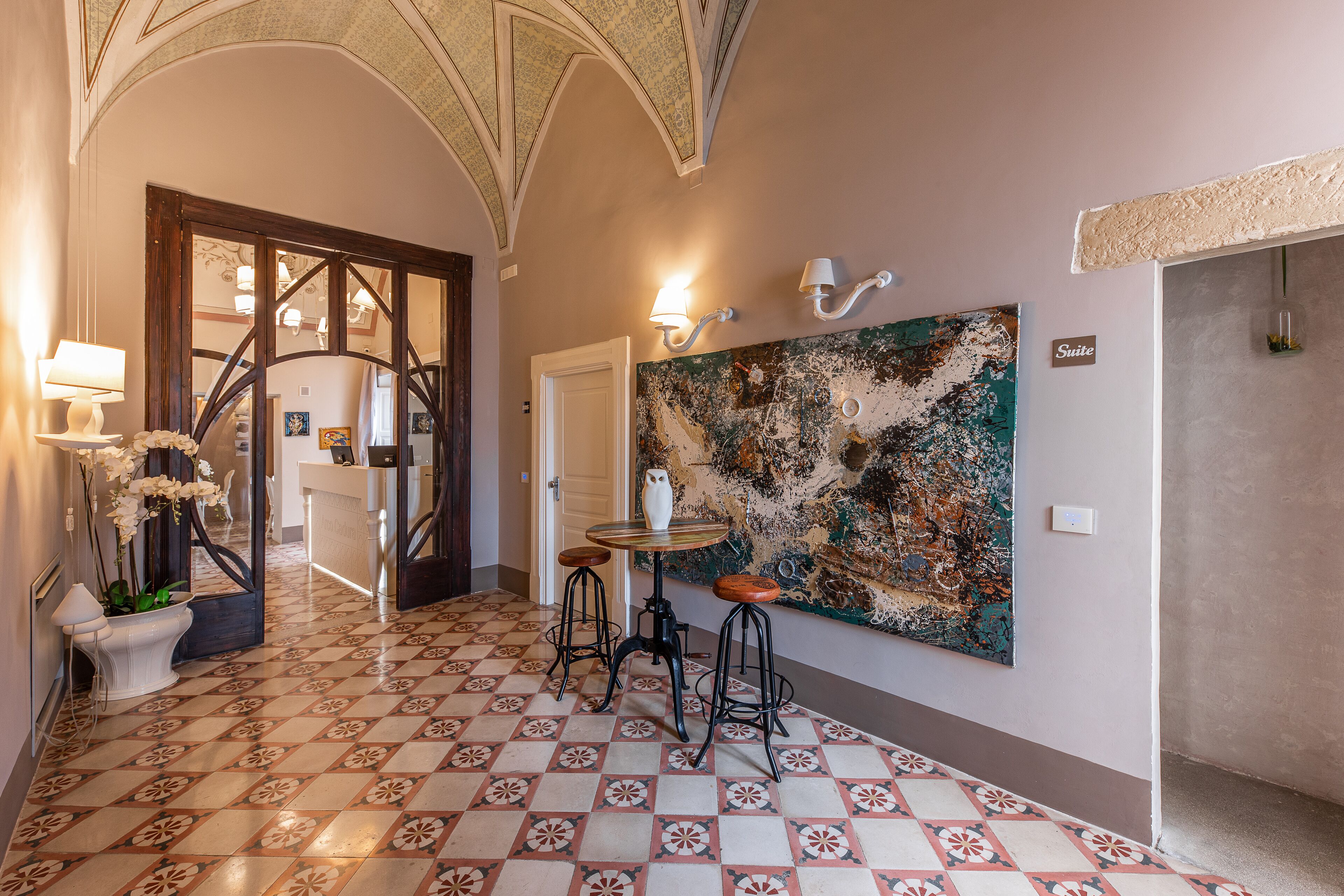 Eine Hotelhalle mit Fliesenboden, einer Rezeption, einer Bar und einem großen, abstrakten Gemälde an der Wand.