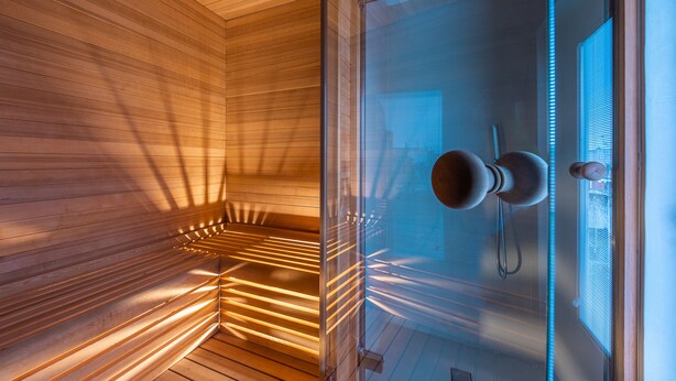 Uma sauna com ripas de madeira e porta de vidro, um porta-toalhas e uma janela com persianas.