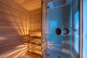 Un sauna avec des parois en bois et une porte en verre, un porte-serviettes et une fenêtre avec des stores.