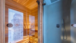 Sala de sauna com paredes de madeira, porta de vidro e área de chuveiro.