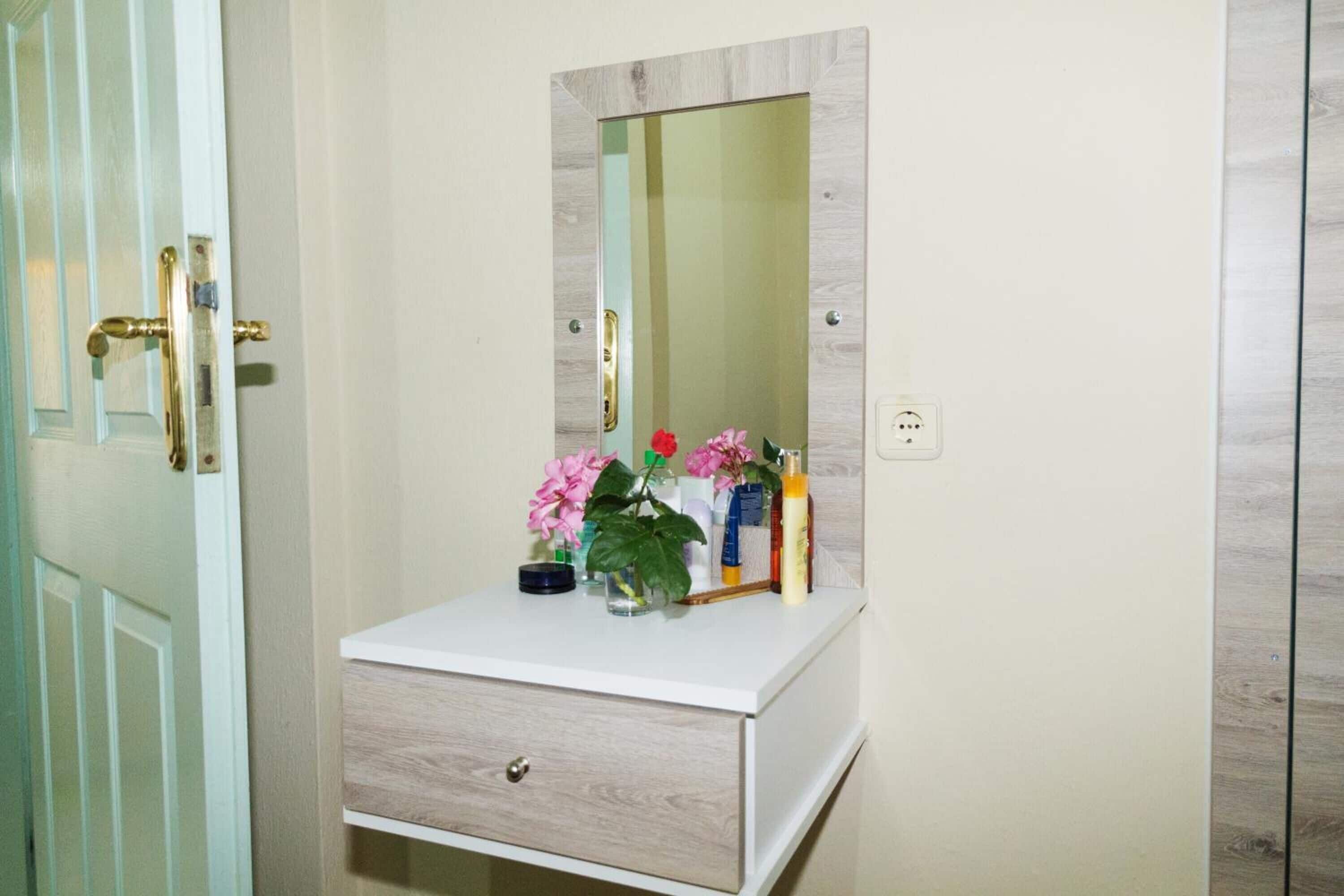 A bathroom vanity with a mirror, a small drawer, and a shelf with toiletries.