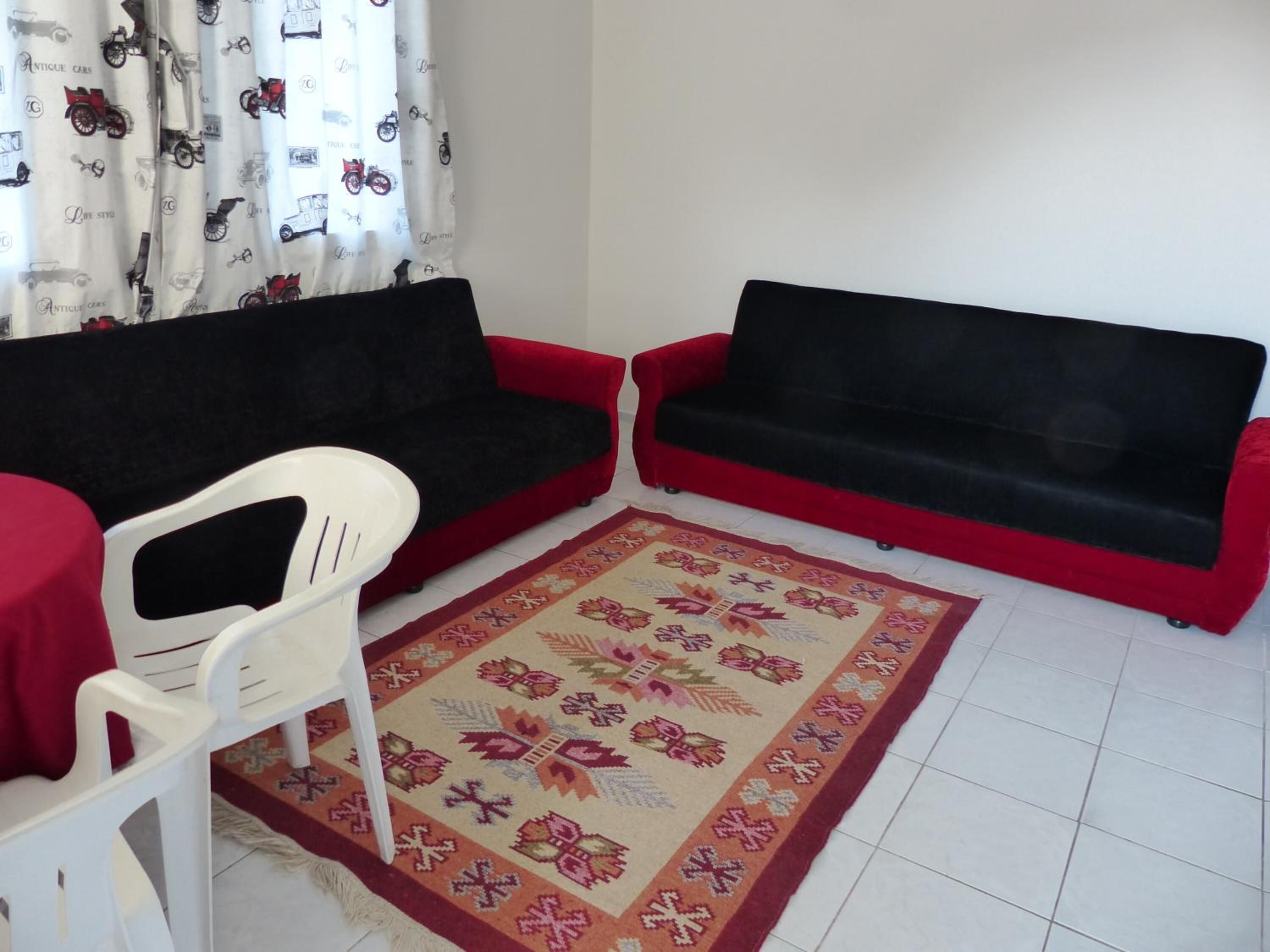 Una sala pequeña con dos sofás rojos, una silla blanca y un tapete estampado.