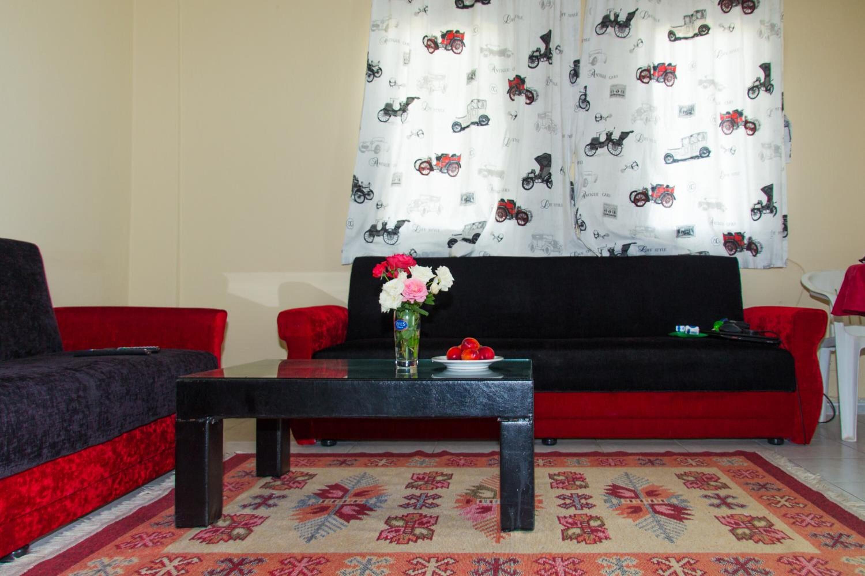 A living room with a black sofa, a red sofa, a glass coffee table, and a patterned rug.