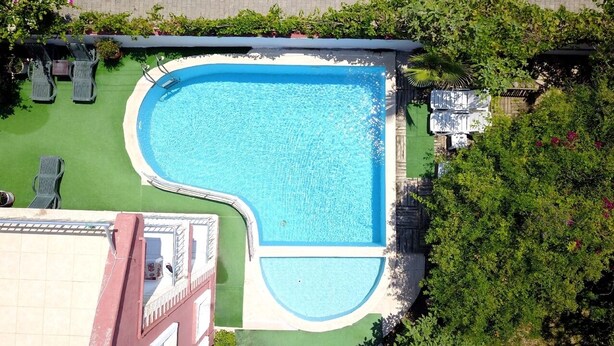 Vista aérea de una piscina de diseño curvo, rodeada de césped verde y sillones de descanso.