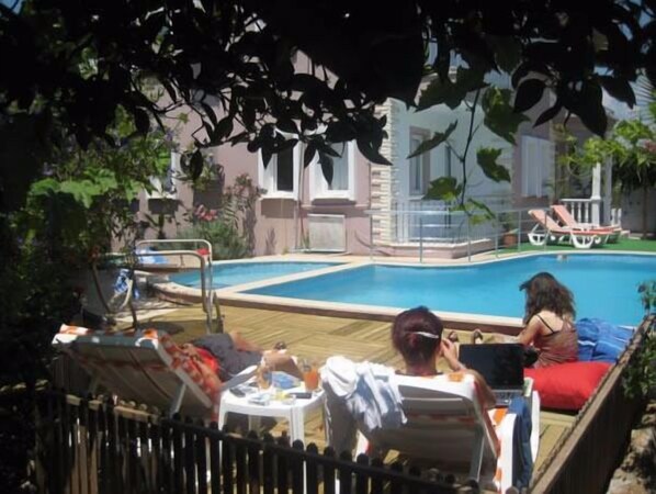 A pool area with lounge chairs and a table, surrounded by greenery and buildings.