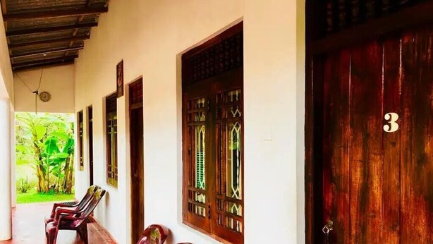 Un pasillo con bancos de madera, una puerta de madera con un número y una ventana con una celosía decorativa.