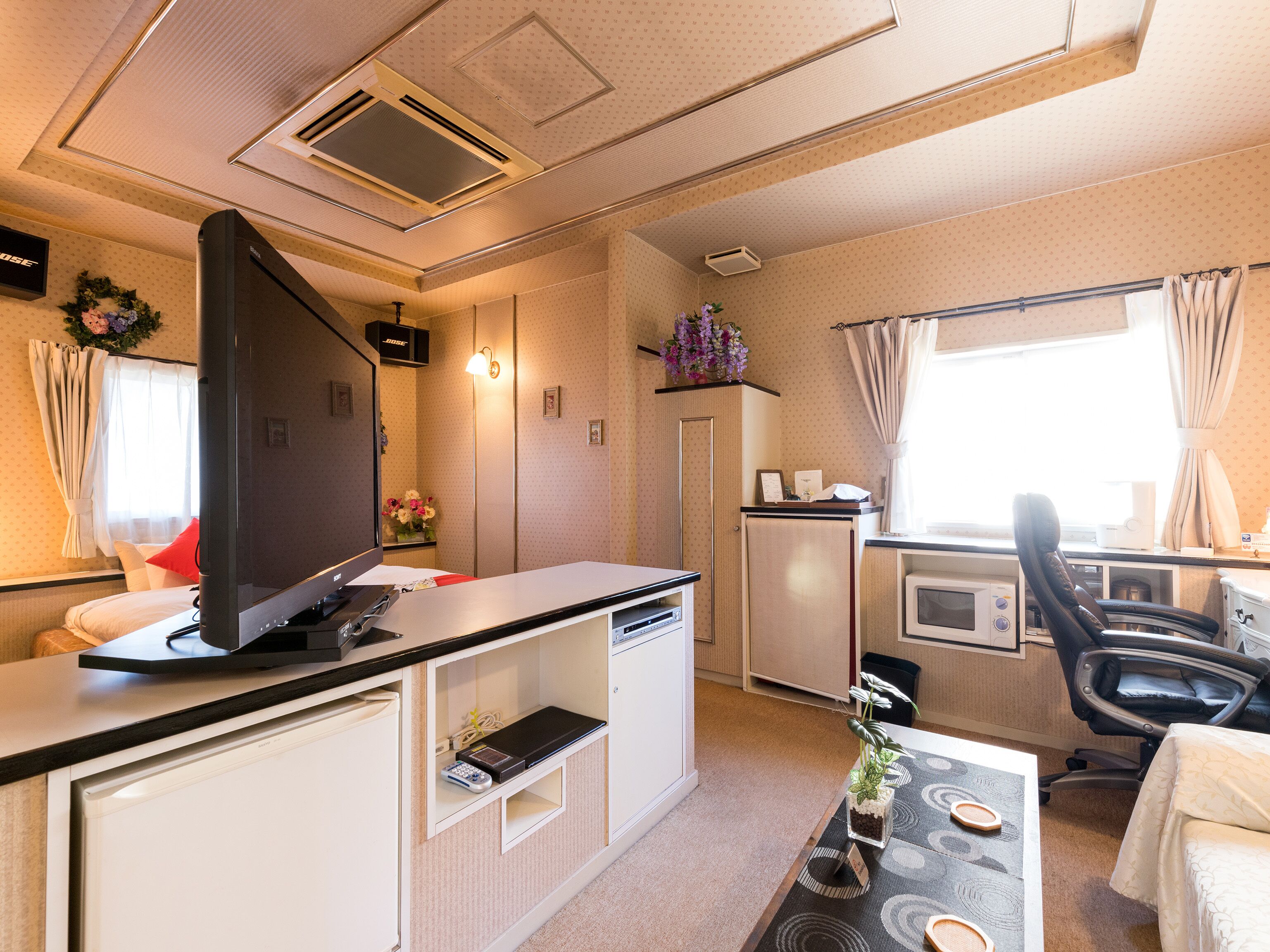 A compact hotel room with a kitchenette, a flat-screen TV, a small refrigerator, a microwave, a coffee maker, and a desk with a chair.