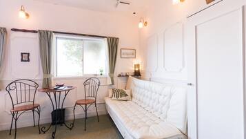 A cozy room with a white sofa, a small table, two chairs, a window with curtains, and wall-mounted lights.