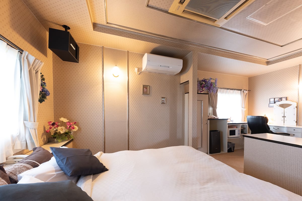 Een hotelkamer met een bed, nachtkastje, lamp, airconditioning en een klein bureau met stoel.
