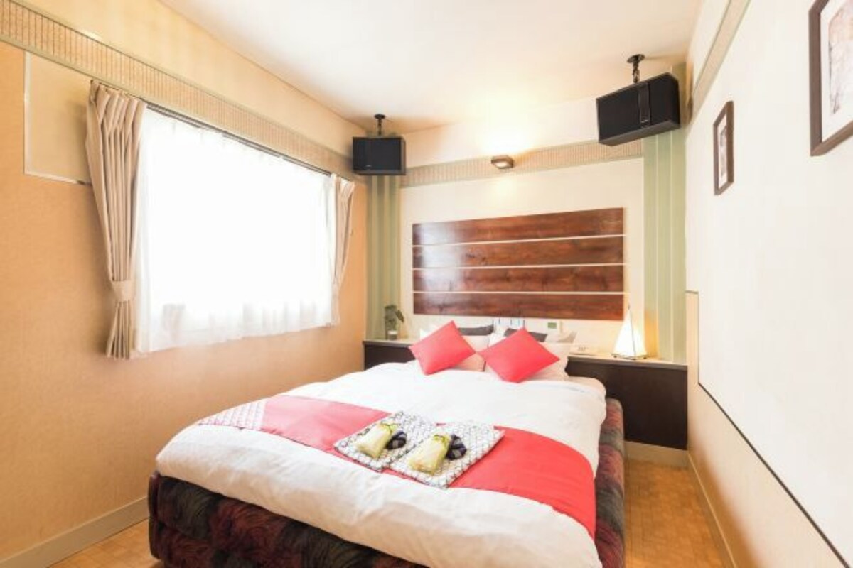 Une chambre d’hôtel avec un lit, une télévision, une table de chevet et une fenêtre avec des rideaux.