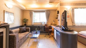 Een gezellige, compacte ruimte met een bank, een glazen salontafel, een bureau met stoel, een televisie en een radiator.