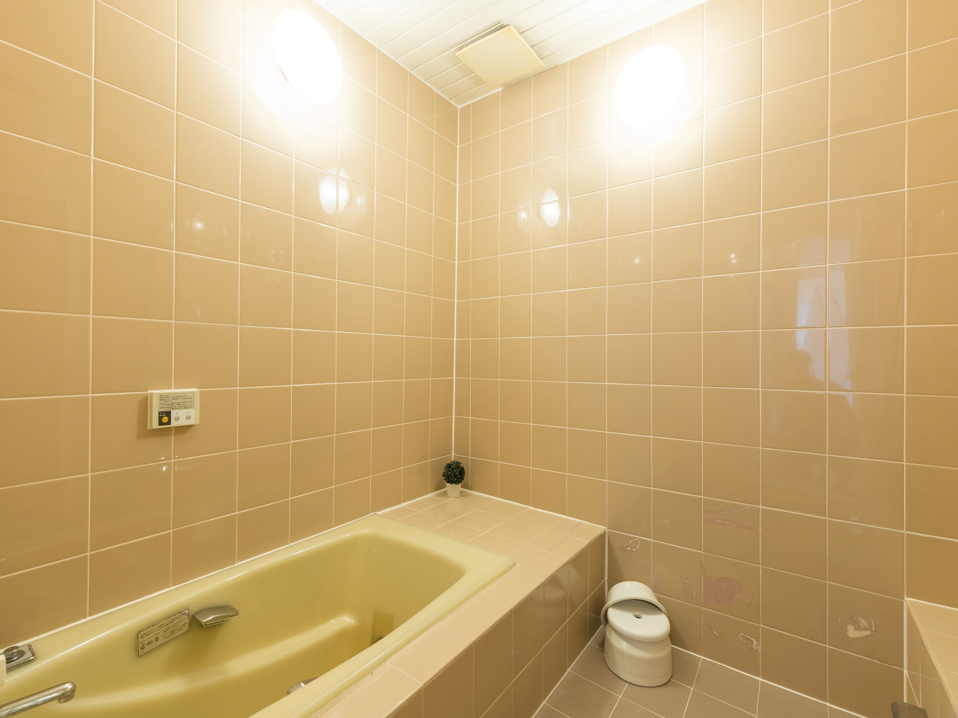 A bathroom with beige tiles, a bathtub, a toilet, and a small potted plant.