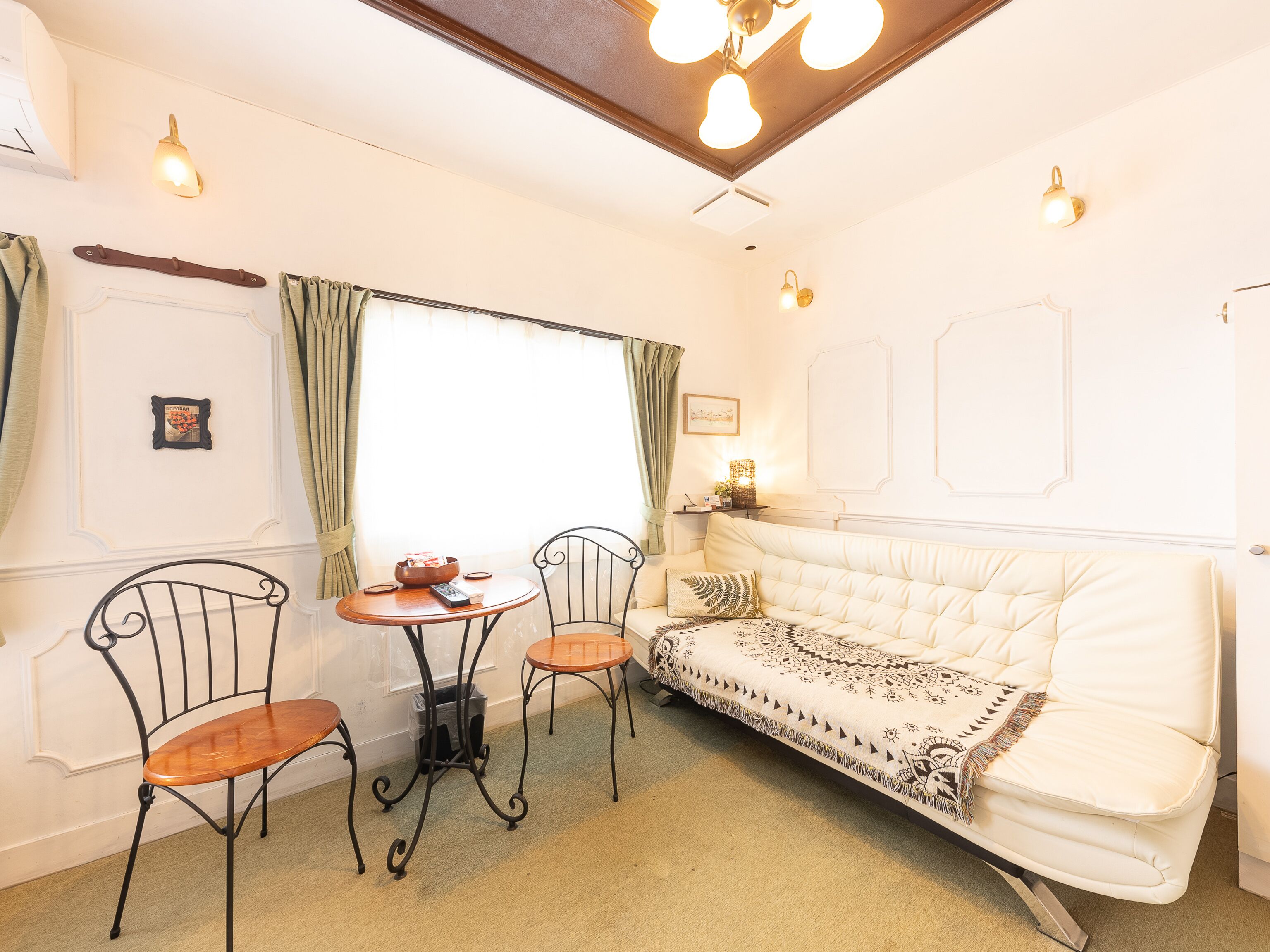 A cozy room with a white sofa, two chairs, a small table, and a window with curtains.